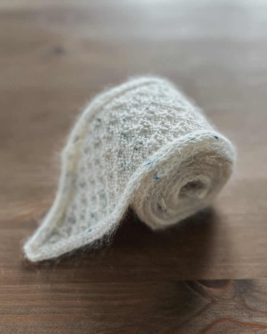 Rullet Granola Scarf i lyst garn med blå stik på et træbord · strikkes frem og tilbage