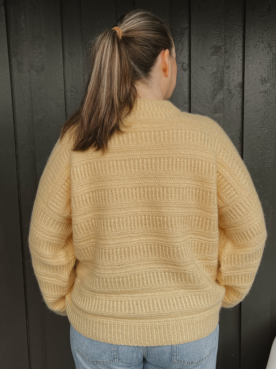 Gul Coffee Sweater bakifrån, strukturen går runt hela bålen · bakstycket stickas i två axeldelar och samlas på stickan