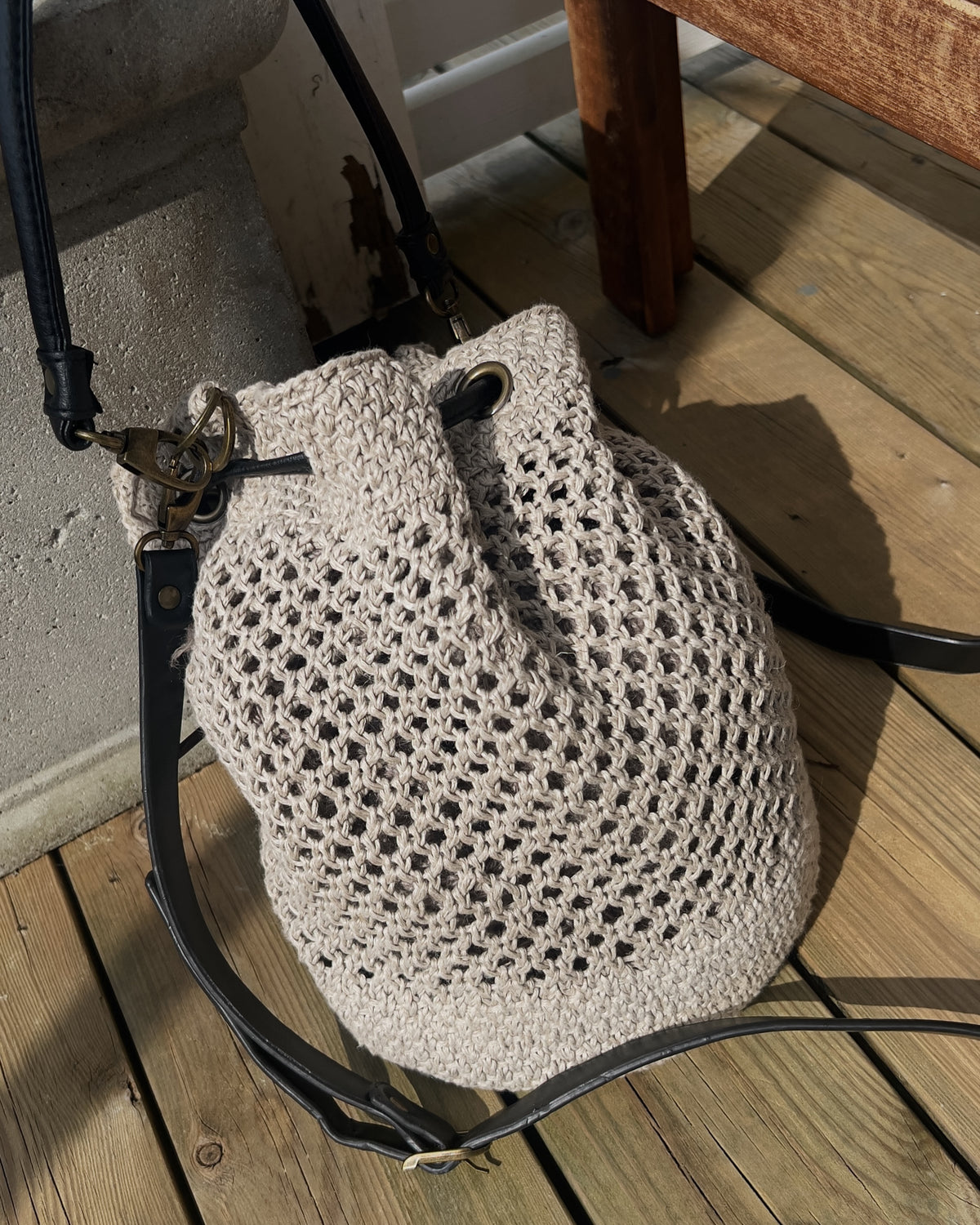 Bucket bag med lang skulderrem på en træterrasse · netmønster på midterpartiet