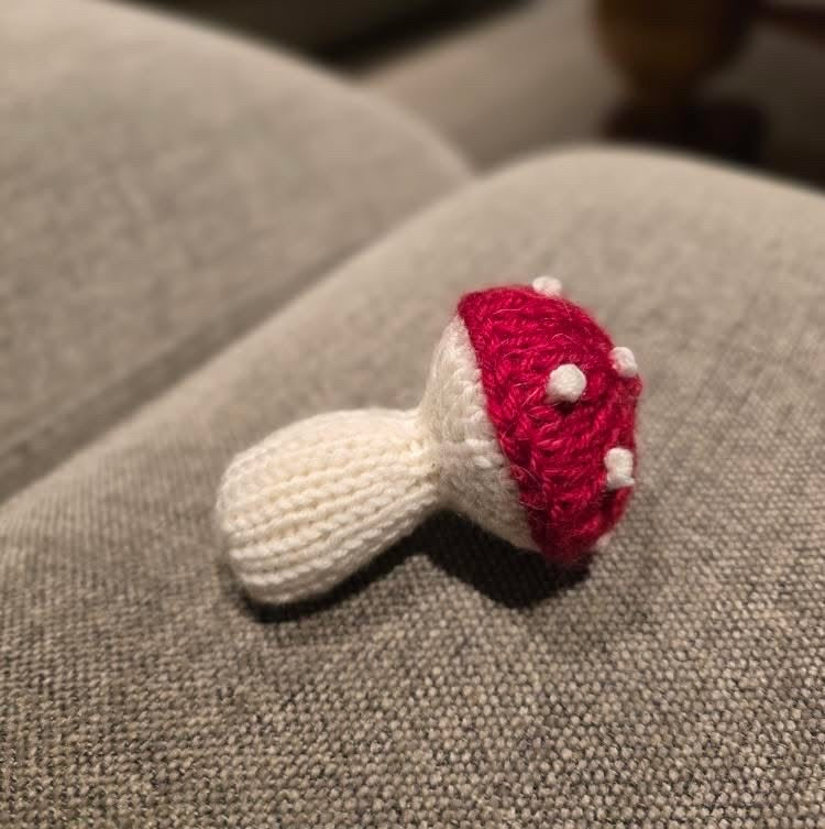 Liten stickad svamp med röd hatt och vita prickar på en grå soffa · vilket garn som helst fungerar