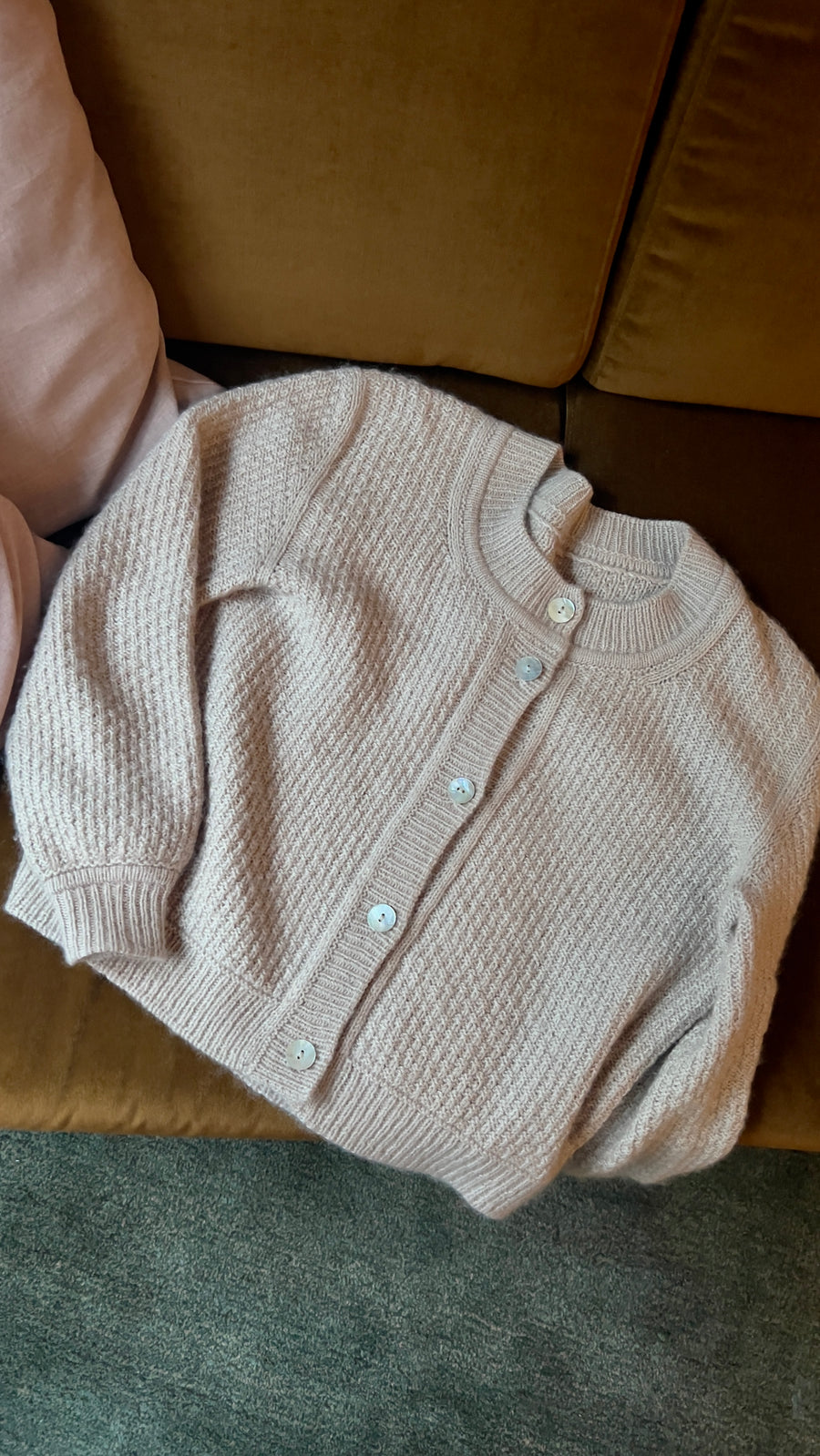 Mistlight Cardigan flatt på en sofa, med perlemorsknapper og struktur · strikkes ovenfra og ned