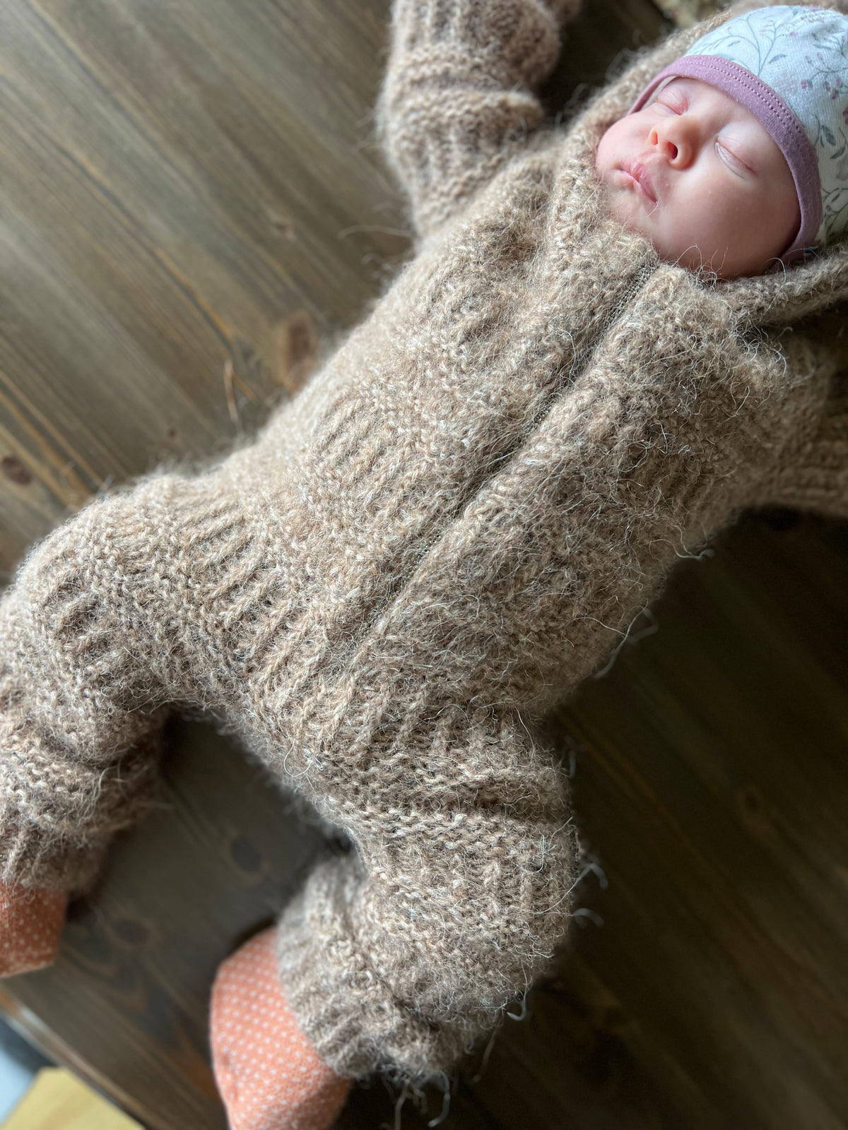Baby i Coffee Onesie på ett träbord, sedd från sidan · resår i dubbel längd kan vikas upp