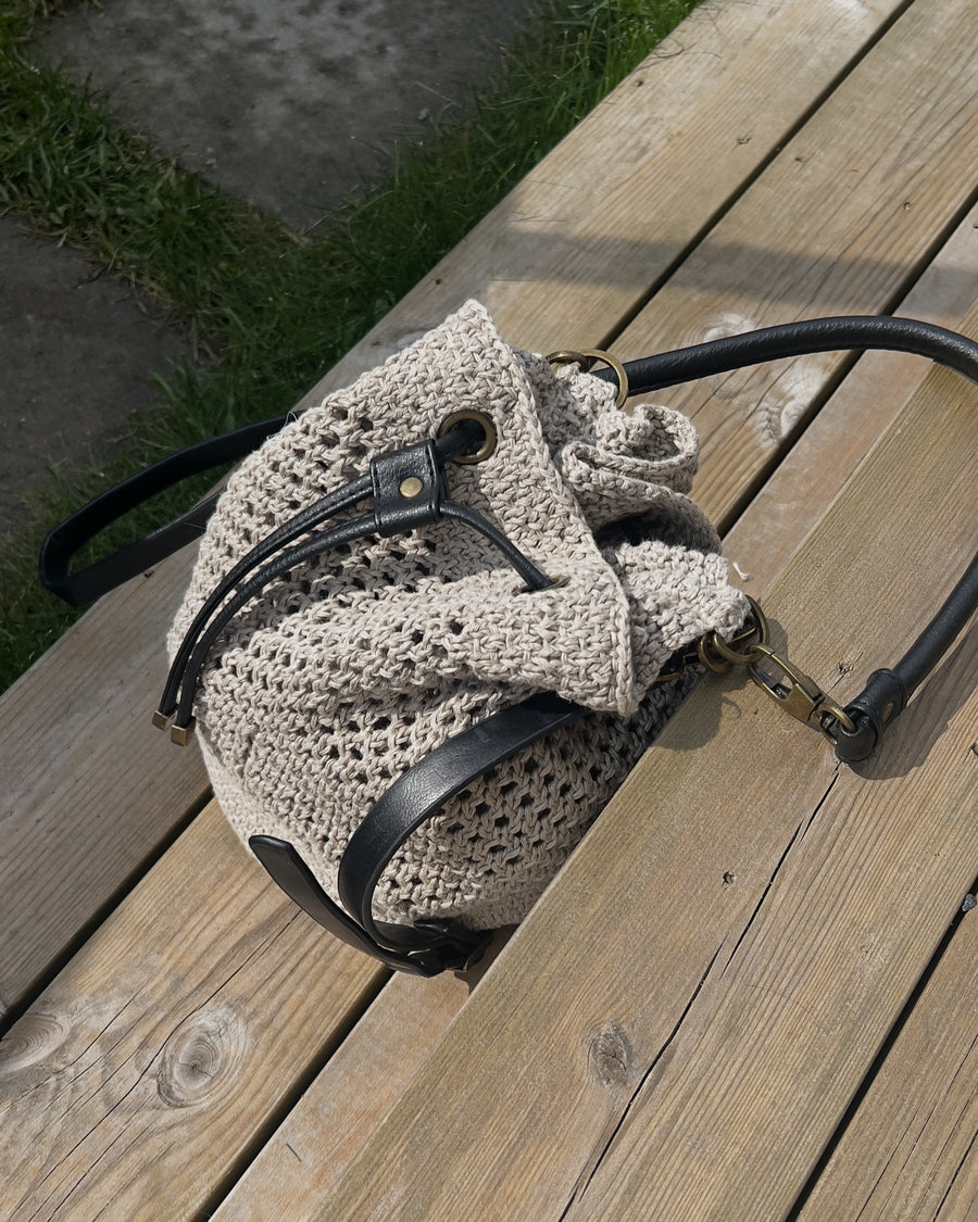 Bucket bagen på siden på træplanker, set oppefra, med snøret trukket sammen · garnet er Hør Organic