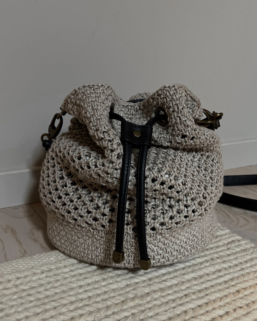 Bucket bag på et vævet tæppe mod en væg, med snøre og messingender · fast bund i to lag