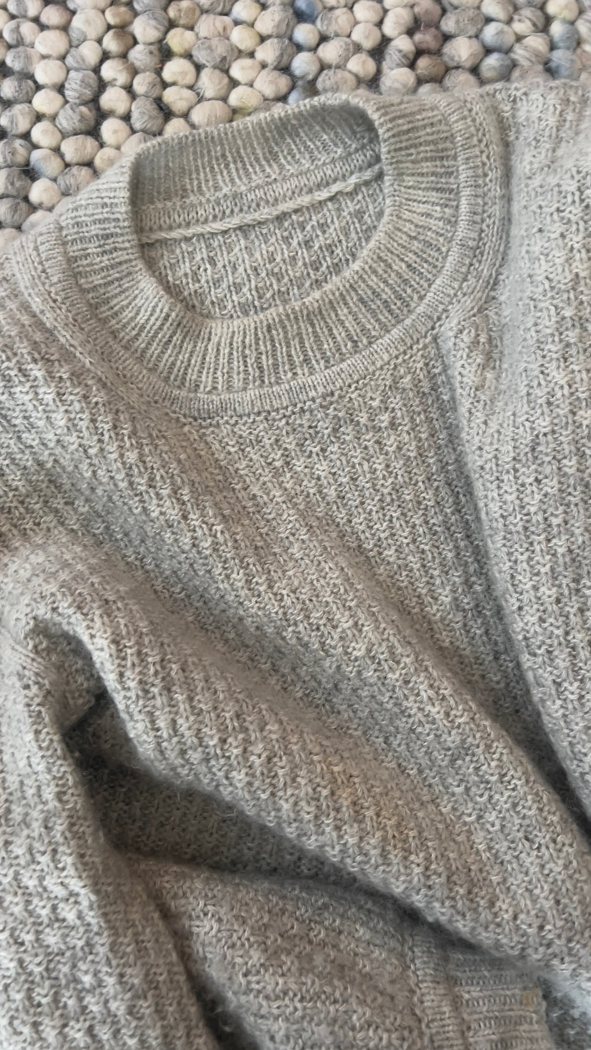 Ribbad halskant och struktur på Mistlight Sweater, liggande på filten · axeldelarna läggs upp var för sig