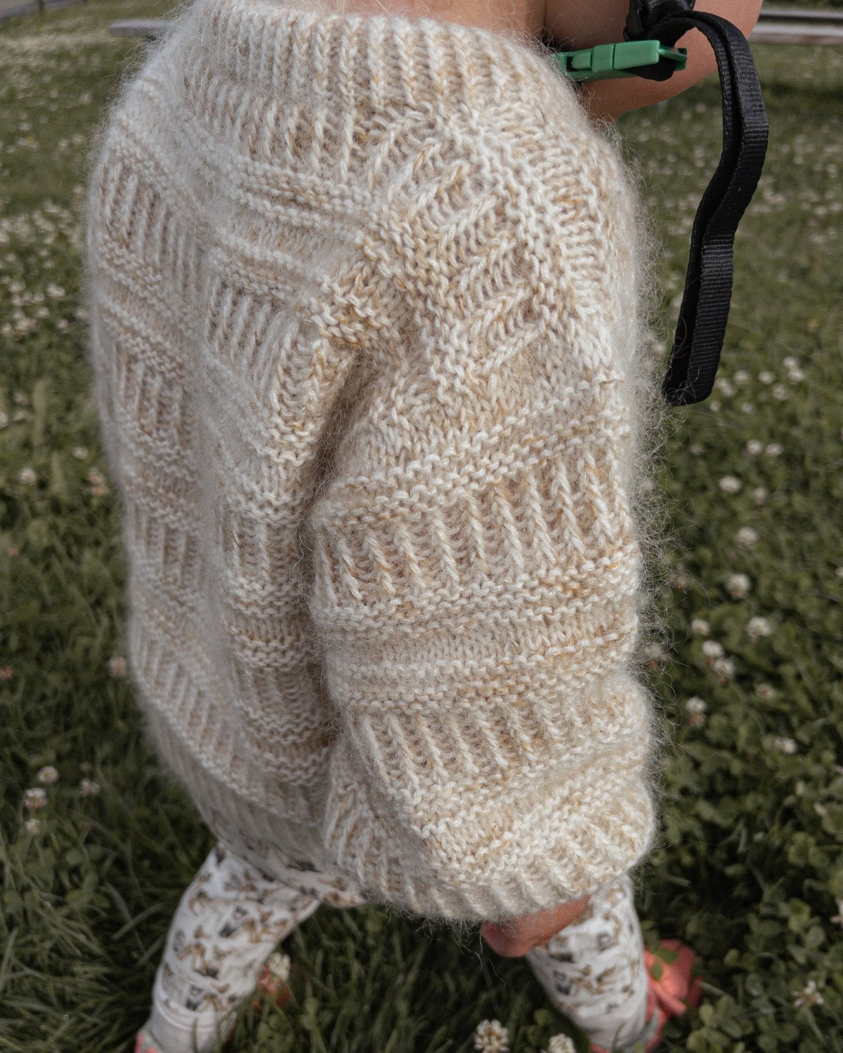 Ärm och sida på Coffee Sweater Mini, i gräset · mjukt garn håller barnet varmt