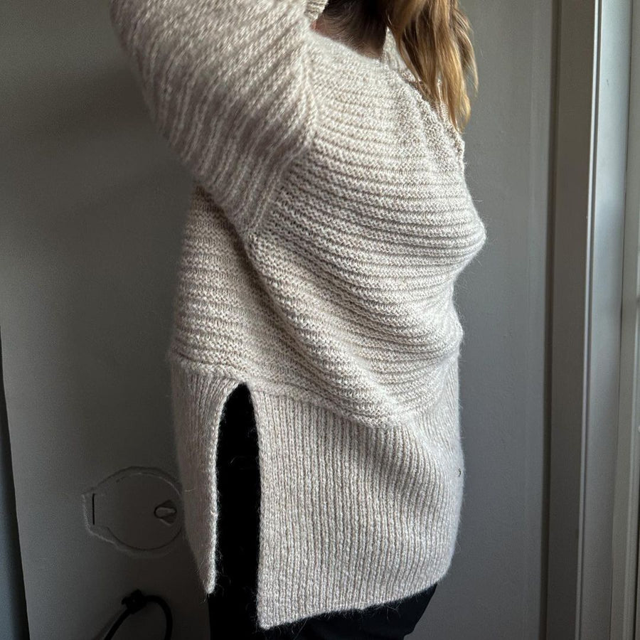 Gräddvit Dawn Sweater sedd från sidan, med slits i den ribbade nederkanten · bålen stickas i ett stycke