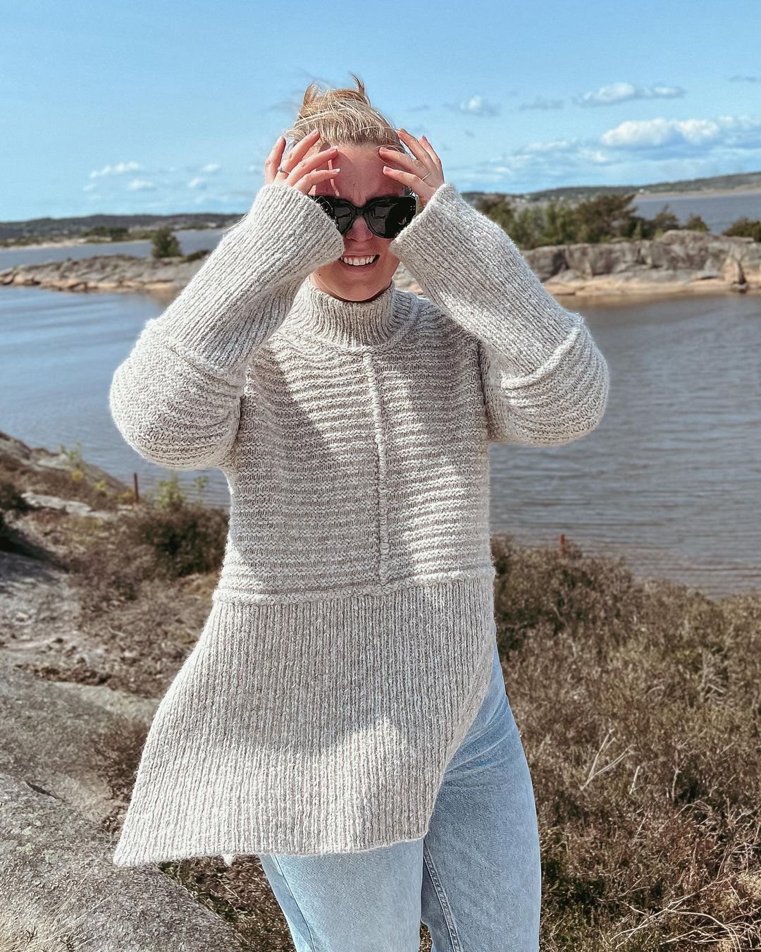 Dawn Sweater utomhus vid havet, med händerna mot ansiktet · stickas uppifrån och ner