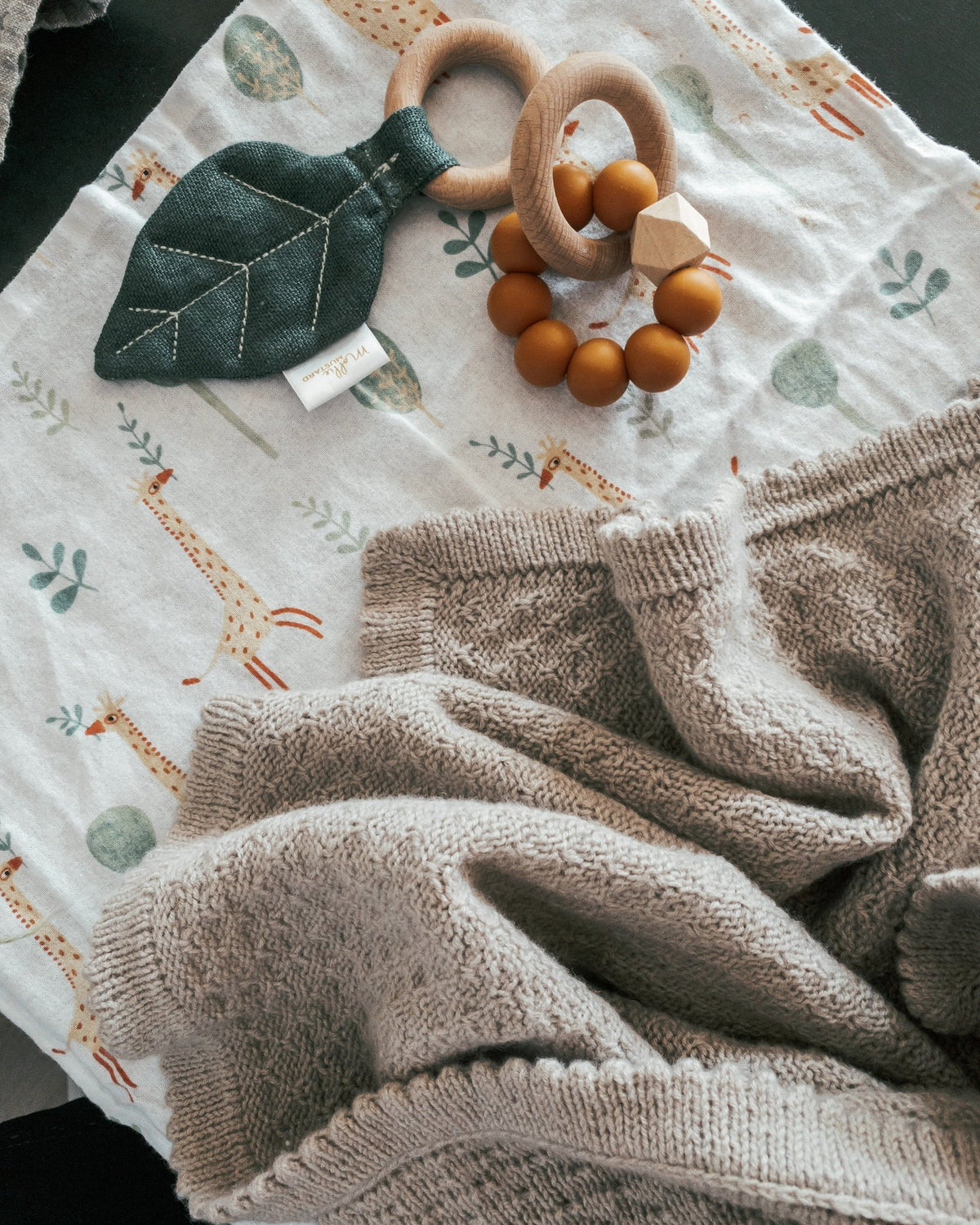 Granola-filt på en duk med giraffmönster och leksaker i trä · samma struktur som Granola Sweater